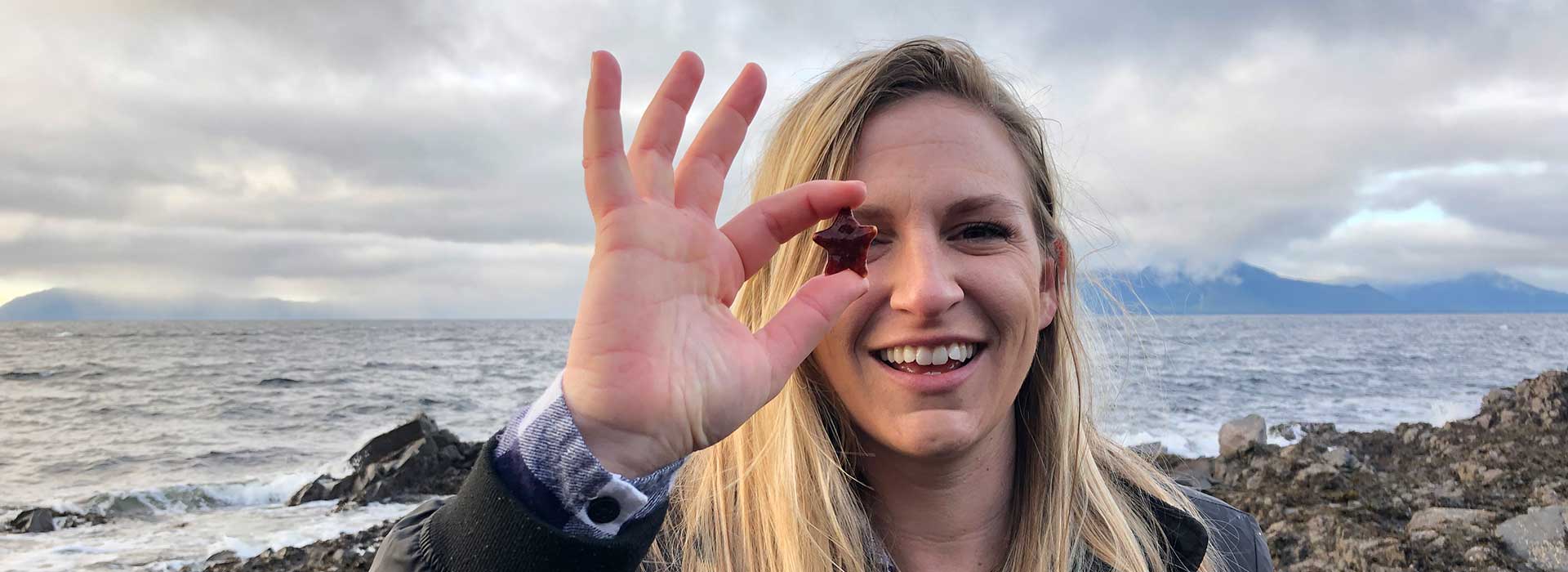 Woman on shore holding star to eye 