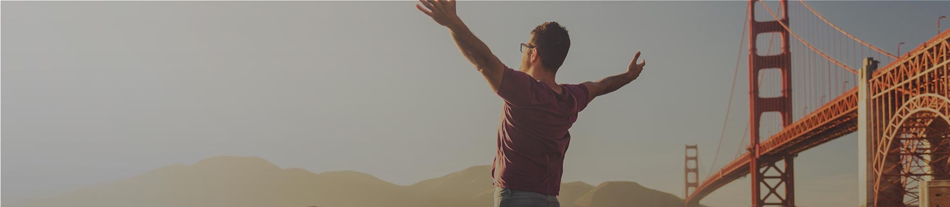 Man looking into distance arms wide open by bridge